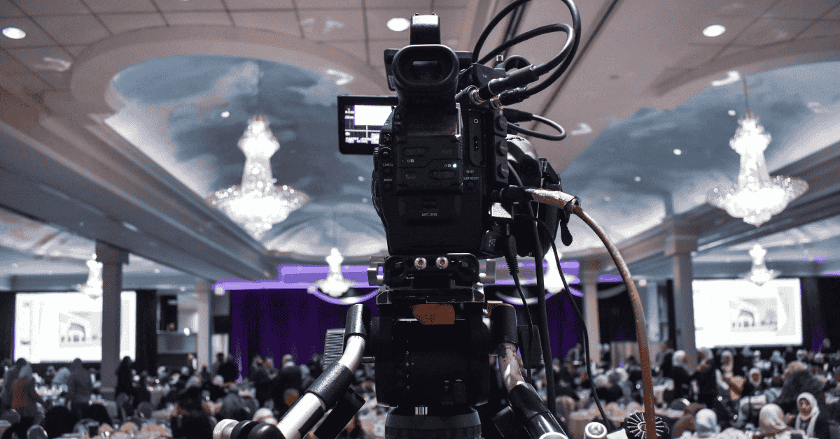 Kamera profesional merekam acara perusahaan besar di ballroom mewah dengan dekorasi elegan, menggambarkan peran penting event organizer dalam mengelola acara dari perencanaan hingga dokumentasi.